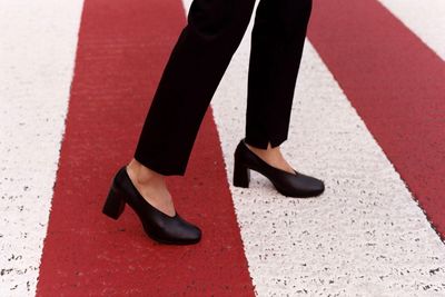 Low section of woman standing in high heels on zebra crossing