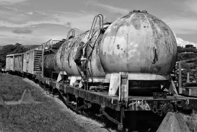 Boy climbing on abandoned freight train on railroad track against sky