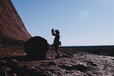 Man with arms raised standing at ayers rock in uluru-kata tjuta national park against sky