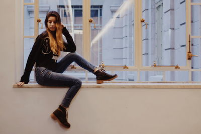 Portrait of young woman sitting against wall