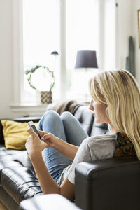 Teenage girl using phone while reclining on sofa at home
