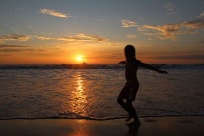 Silhouette boy running at beach against sky during sunset