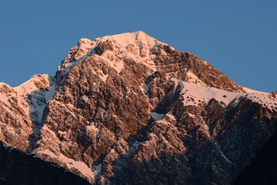 Low angle view of snowcapped mountains against clear blue sky