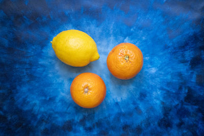 Close-up of two oranges and a lemon on a blue background