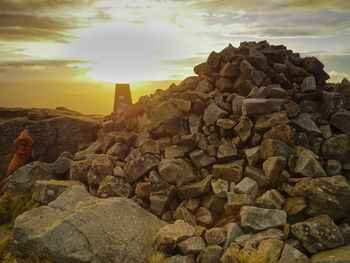 Woman on rocks against sky during sunset