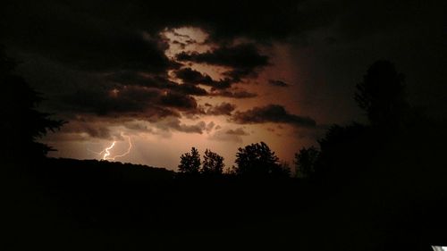 Low angle view of silhouette trees against storm clouds