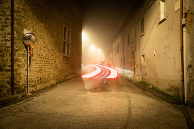 Empty road amidst buildings in city at foggy night