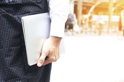 Midsection of businessman holding laptop while standing outdoors