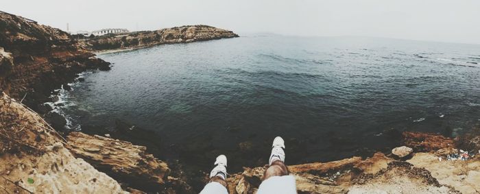 Low section of man on rock by sea against clear sky