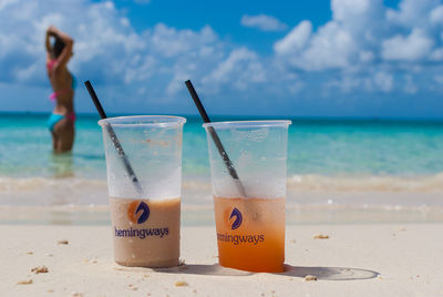 Close-up of drinking glass on sand at beach against sky