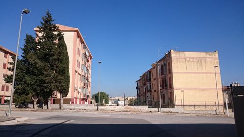 Road leading towards buildings against clear blue sky