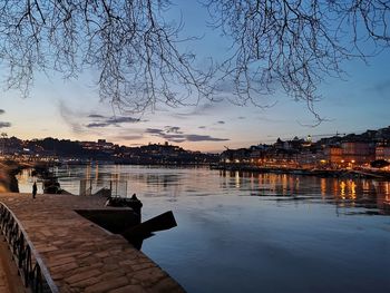 River by illuminated buildings against sky at sunset