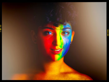 Portrait of young woman with multi colored face against black background