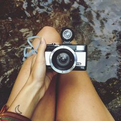 Midsection of woman holding vintage camera over water