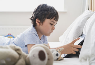 Cute boy using digital tablet while lying on bed at home