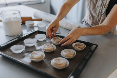 View of woman's hands putting raw cinnamon bun into cupcake case