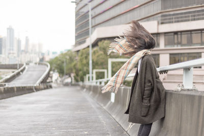 Side view of woman with tousled hair leaning by railing on road