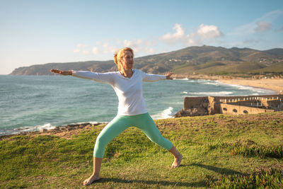 Side view of woman doing yoga on beach against sky