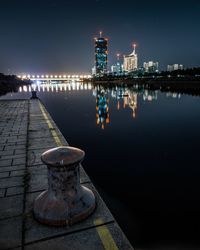 Illuminated cityscape by river against sky at night