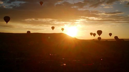 Silhouette hot air balloon flying over landscape against sky during sunset