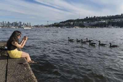 Woman photographing ducks at riverbank in city