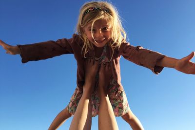 Low section of mother legs balancing happy daughter against clear blue sky