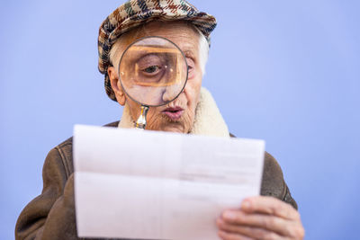 Close-up of senior woman examining paper with magnifying glass against blue background