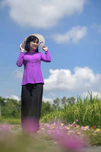 Woman standing by pink flower on field against sky