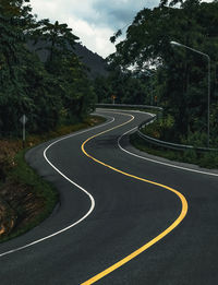 Empty road by trees in city against sky