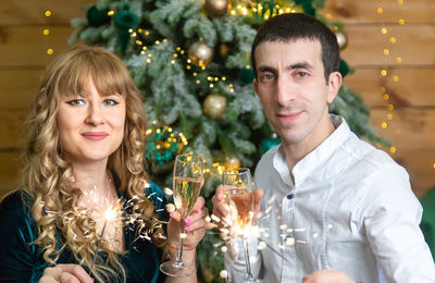 Portrait of smiling woman with man standing against christmas tree