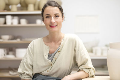 Portrait of smiling mid adult potter sitting in workshop