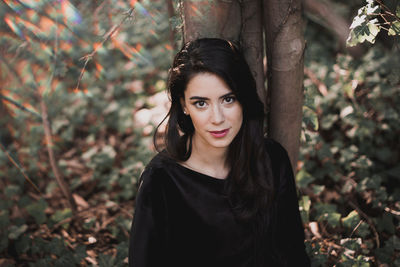 Portrait of young woman standing against tree trunk