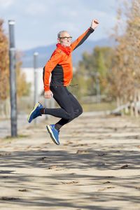 Portrait of senior man jumping on road during autumn
