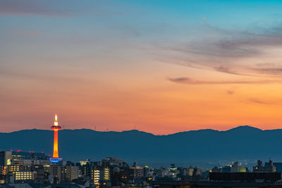 Illuminated buildings in city against romantic sky at sunset