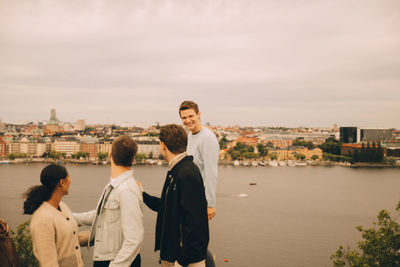 Portrait of friends standing by river in city against sky
