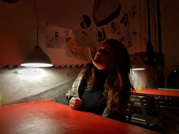 Young woman sitting at table by wall