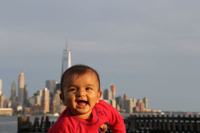 Cute cheerful baby boy looking away against buildings in city