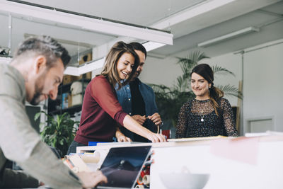 Smiling businesswoman working with colleagues while businessman using laptop in creative office