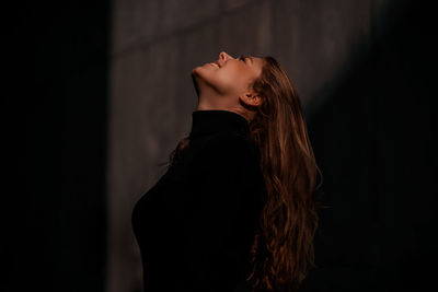 Side view of woman with long hair looking up while standing outdoors at night