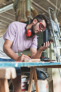 Young male carpenter using smart phone while working in workshop