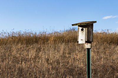 Old birdhouse and grass on field against sky