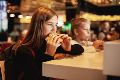 Beautiful schoolgirl eating hamburger sitting in a cafe 