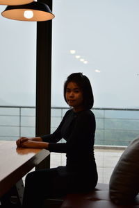 Portrait of young woman sitting on sofa by table against window in cafe