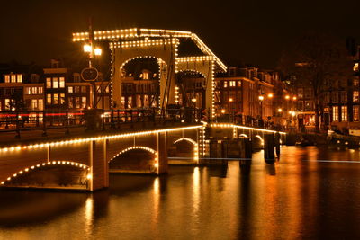 Illuminated bridge over river in city at night