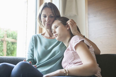 Mother comforting daughter sitting on sofa