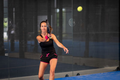 Woman playing padel in a blue grass paddle court indoor - sporty woman padel player hitting ball