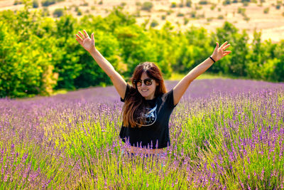 Portrait of young woman with arms raised on field