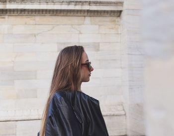 Side view of young woman looking away against wall