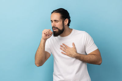 Side view of young man using mobile phone against blue background