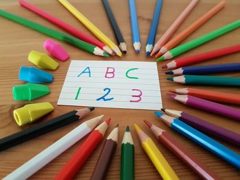 High angle view of multi colored pencils by alphabets and numbers over paper and erasers on table